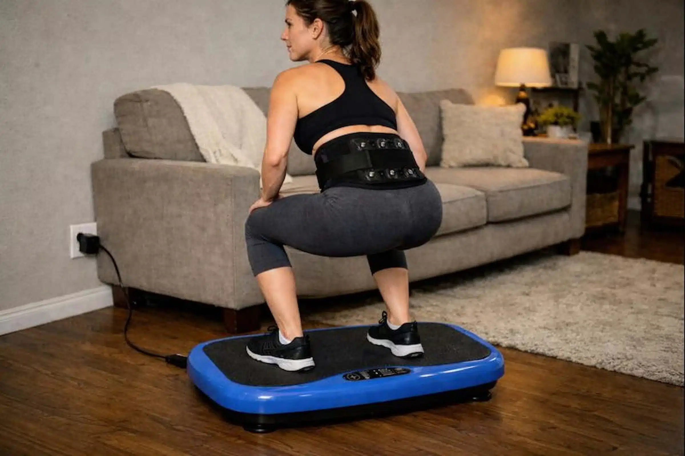 A woman on a vibration plate in a half squat wearing magnetic support lower back pain belt A woman on a vibration plate in a half squat wearing magnetic support lower back pain belt